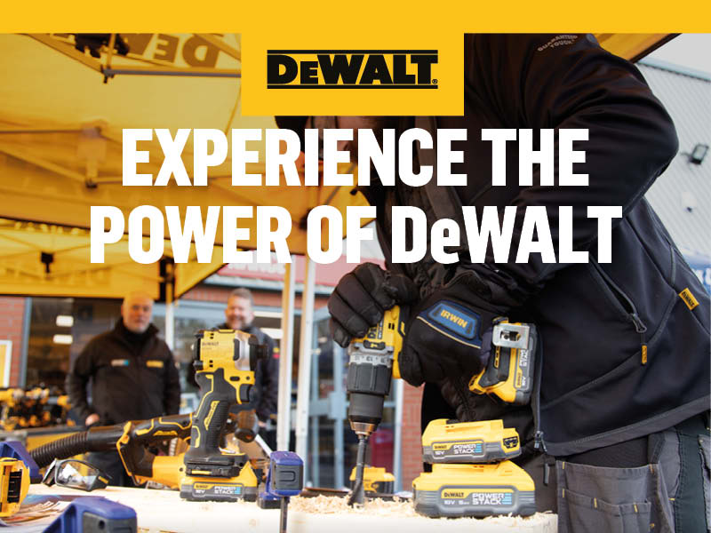 Man wearing gloves using a DeWALT power tool on a bench with other power tools and batteries around.
