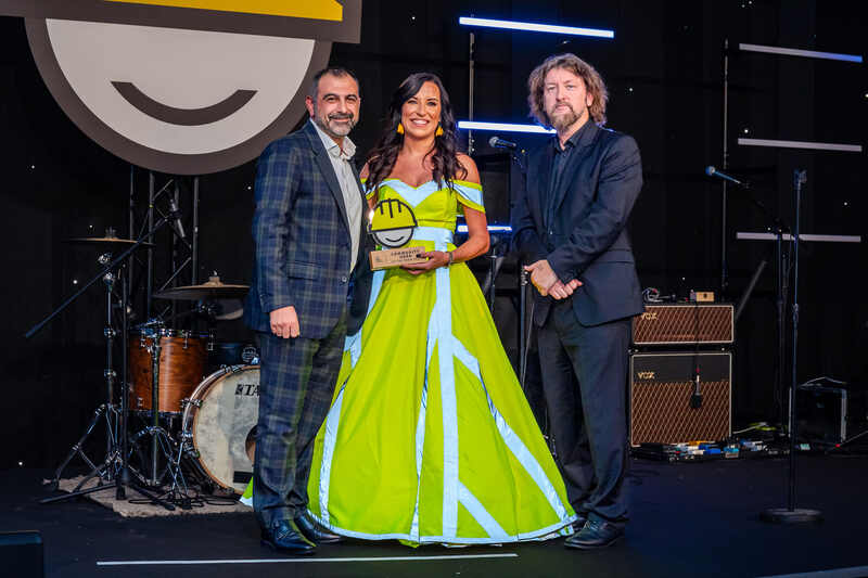 Community Hero Award winner Kelly Cartwright wears a ball gown made from yellow hi vis material, collects her award on stage at the On The Tools Award ceremony