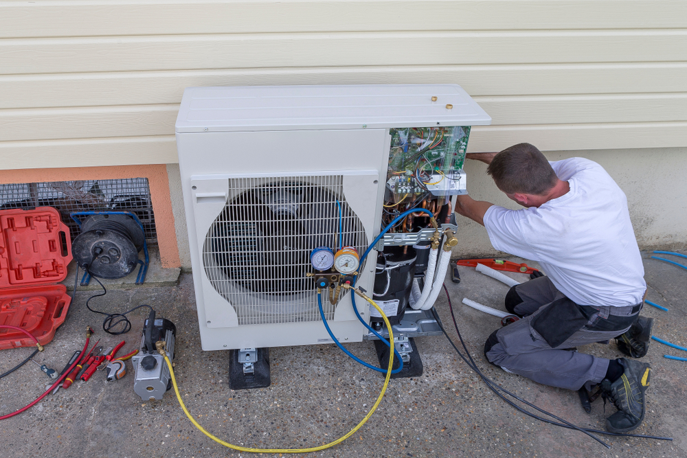 Worker installing heat pump outside a house