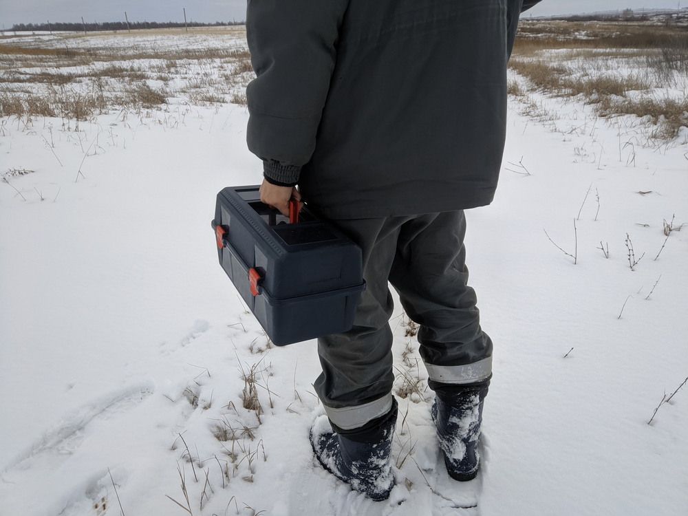 Worker carrying a toolbox over a snowy field