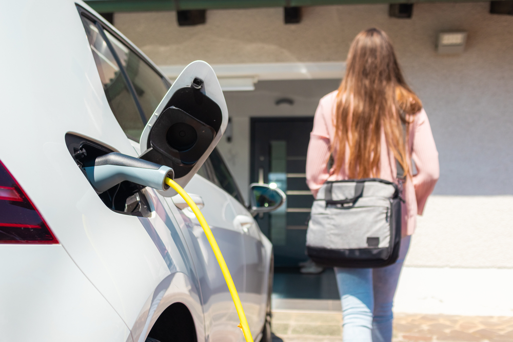 Electric car charger plugged in, with a female silhouette in the background